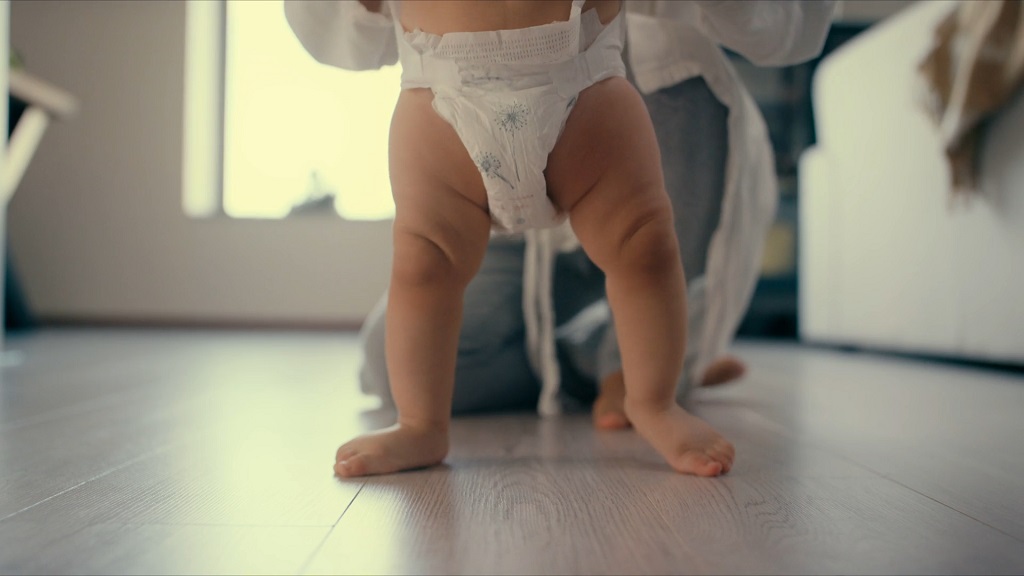 Beba u pelenama pravi prve korake po podu, dok je roditelj pridržava