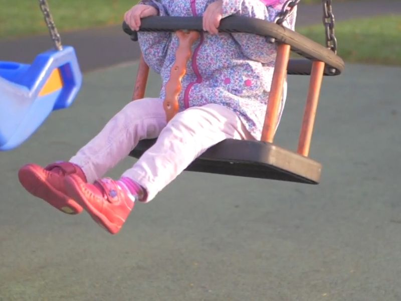 devojčica sedi na ljuljašci u zimskim patofnicama i odeći i ljulja se